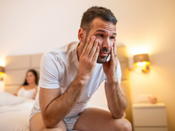 A man looking sad on the edge of his bed while suffering with erectile dysfunction, or going soft during sex