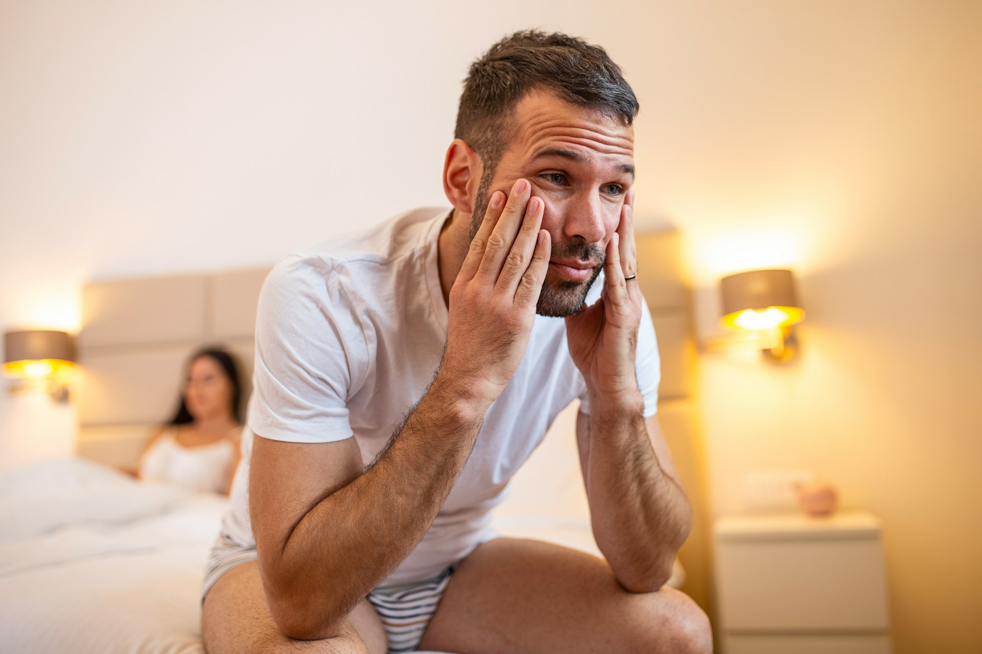 A man looking sad on the edge of his bed while suffering with erectile dysfunction, or going soft during sex