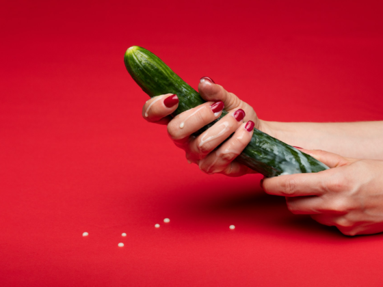 Someone holding a green cucumber with white liquid pouring down it