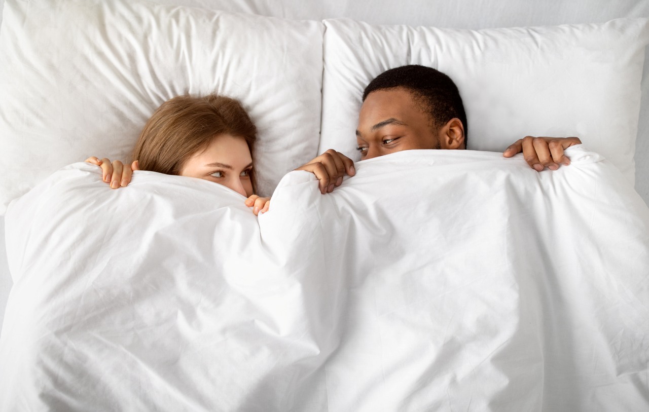 couple hiding under white blanket in bed, looking at each other with affection