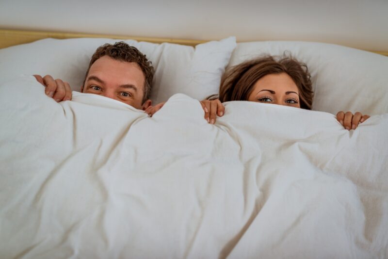 couple in bed hiding under a blanket