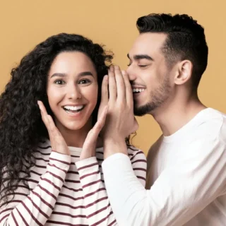 smiling man whispering to a pretty woman with an excited look on her face