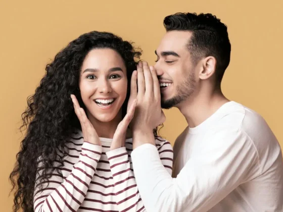 smiling man whispering to a pretty woman with an excited look on her face
