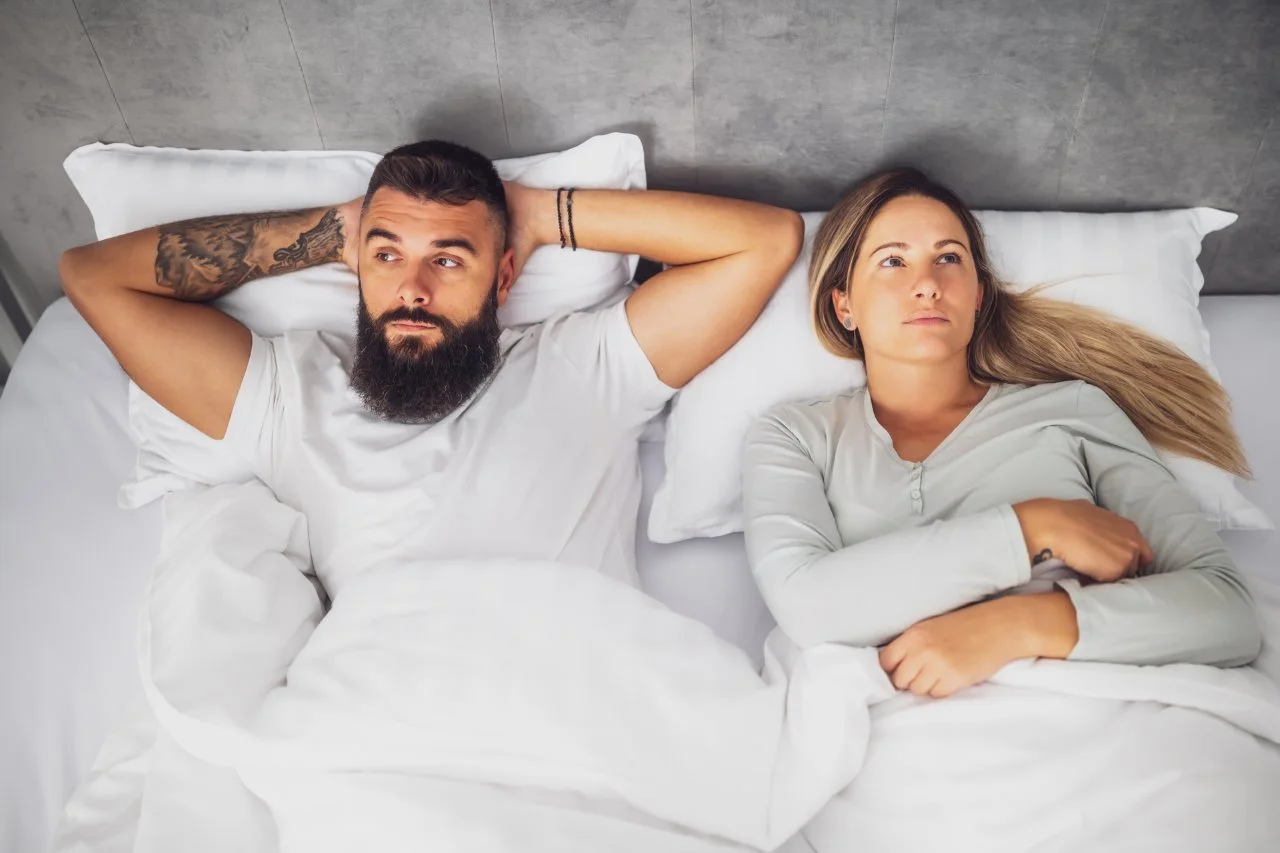 couple lying apart in bed, visibly frustrated and upset